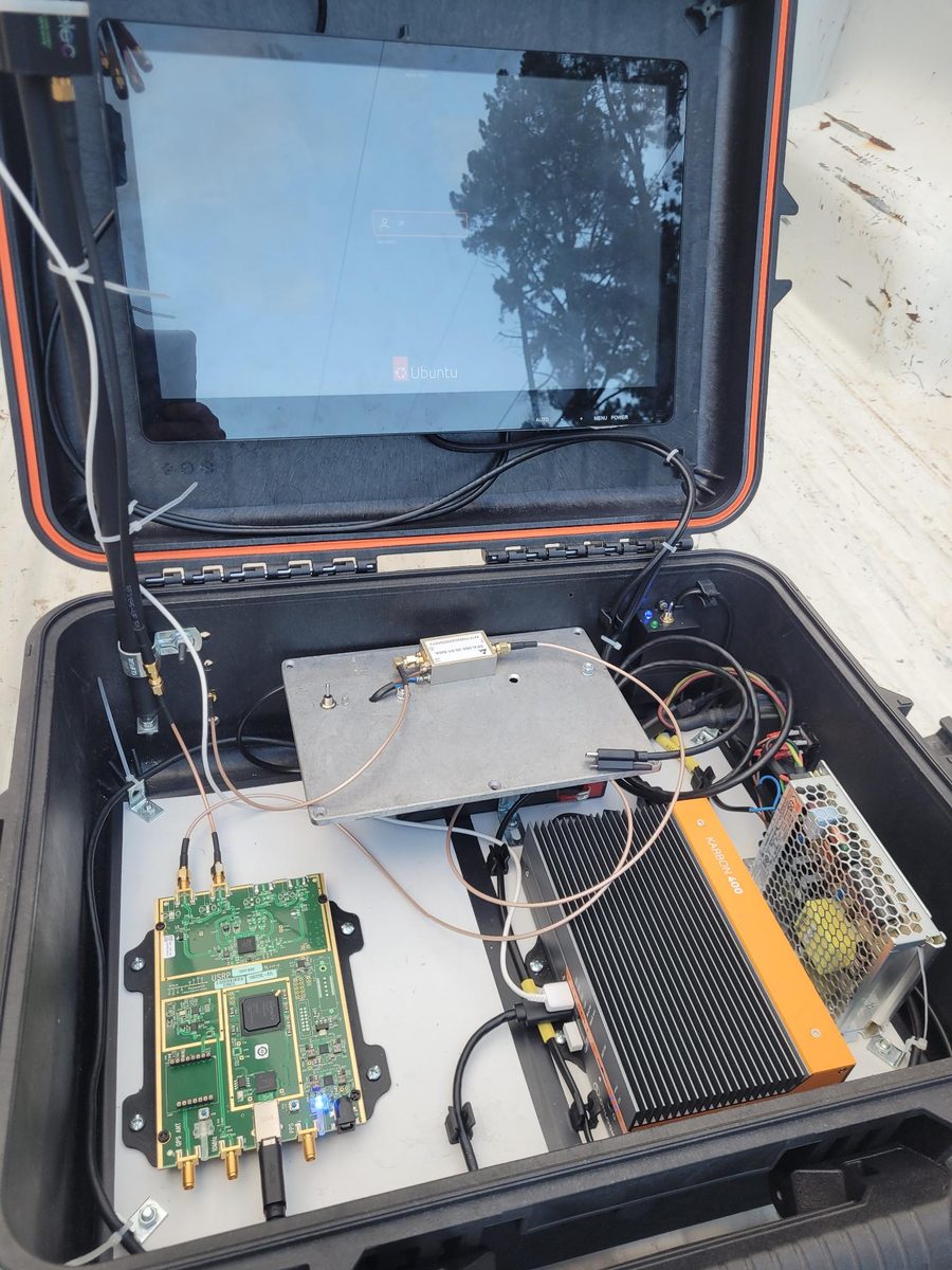 An open transit case containing an RF board, heatsinked module and antenna cabling, set up outdoors.