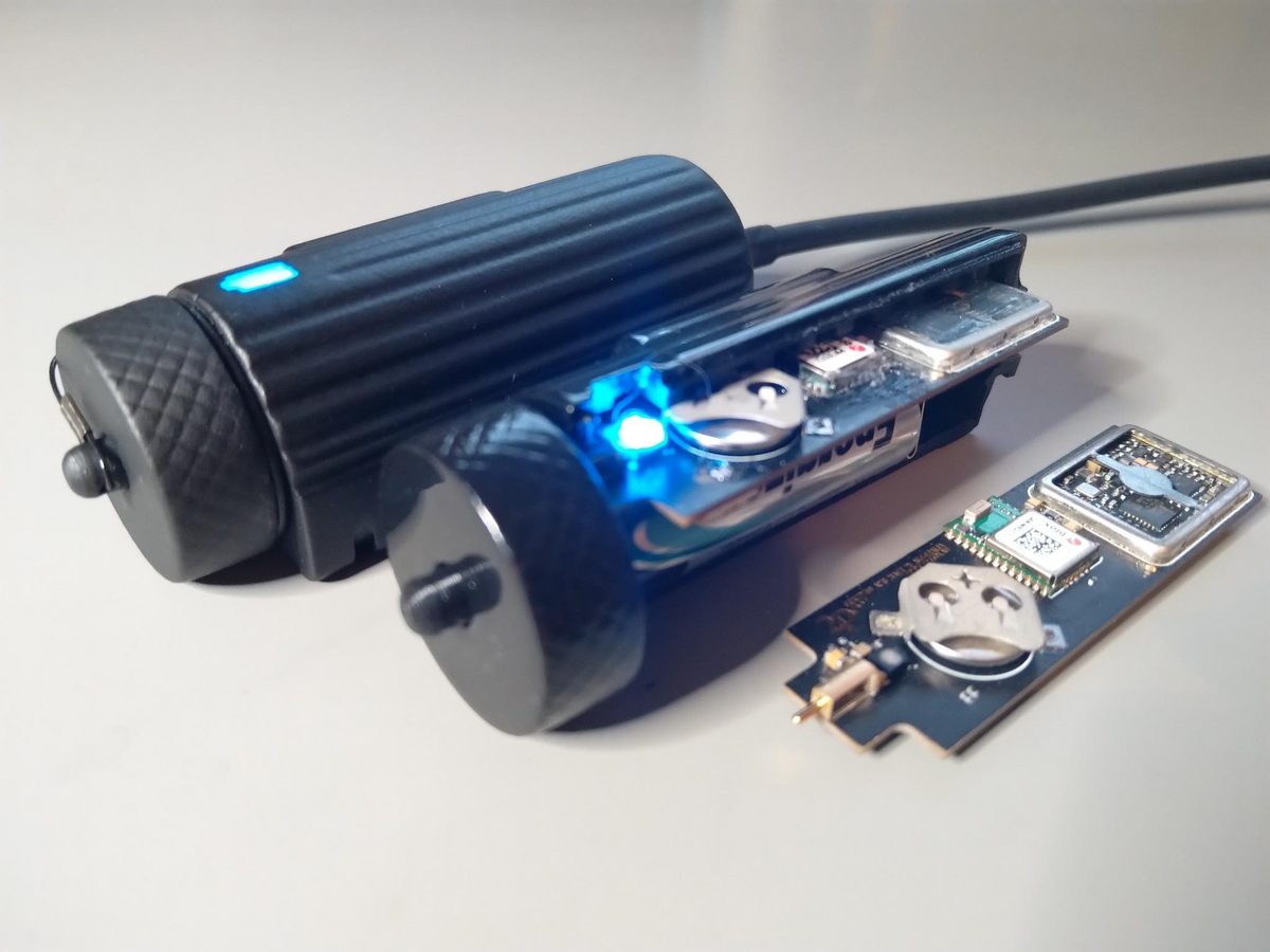 A rugged handheld locator with a ribbed black body and blue indicator, shown beside its internal board carrying a GNSS module and coin cell.