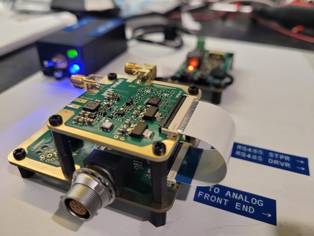 A green circuit board on gold standoffs with a coaxial connector and SMA launch, wired to test equipment, labelled 'TO ANALOG FRONT END'.