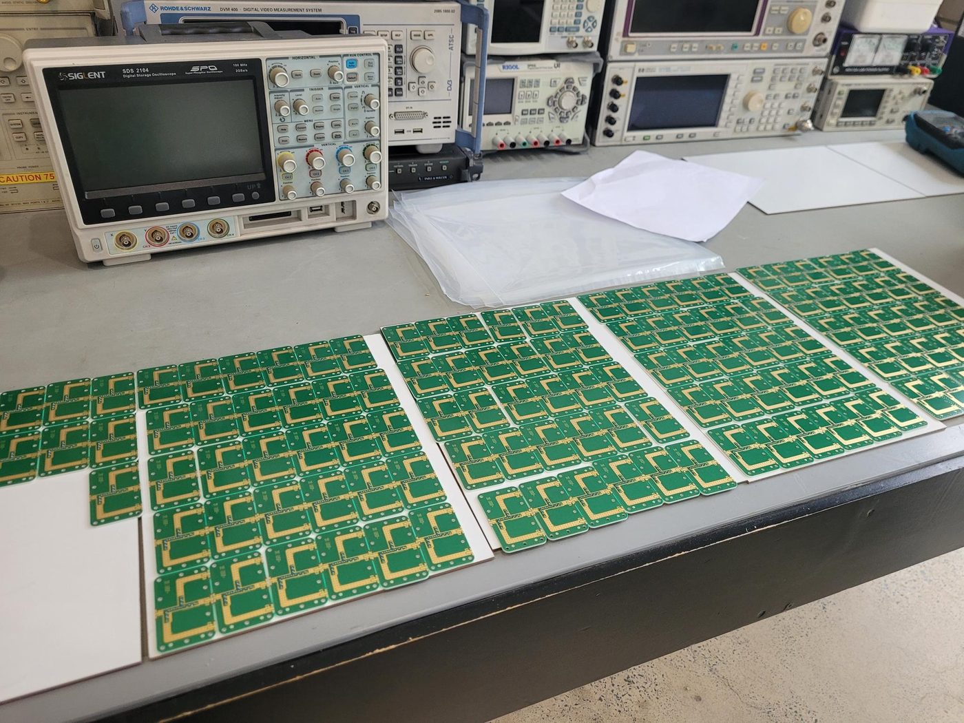 Dozens of small green microwave circuit boards with gold-plated filter structures, laid out in rows on a bench.